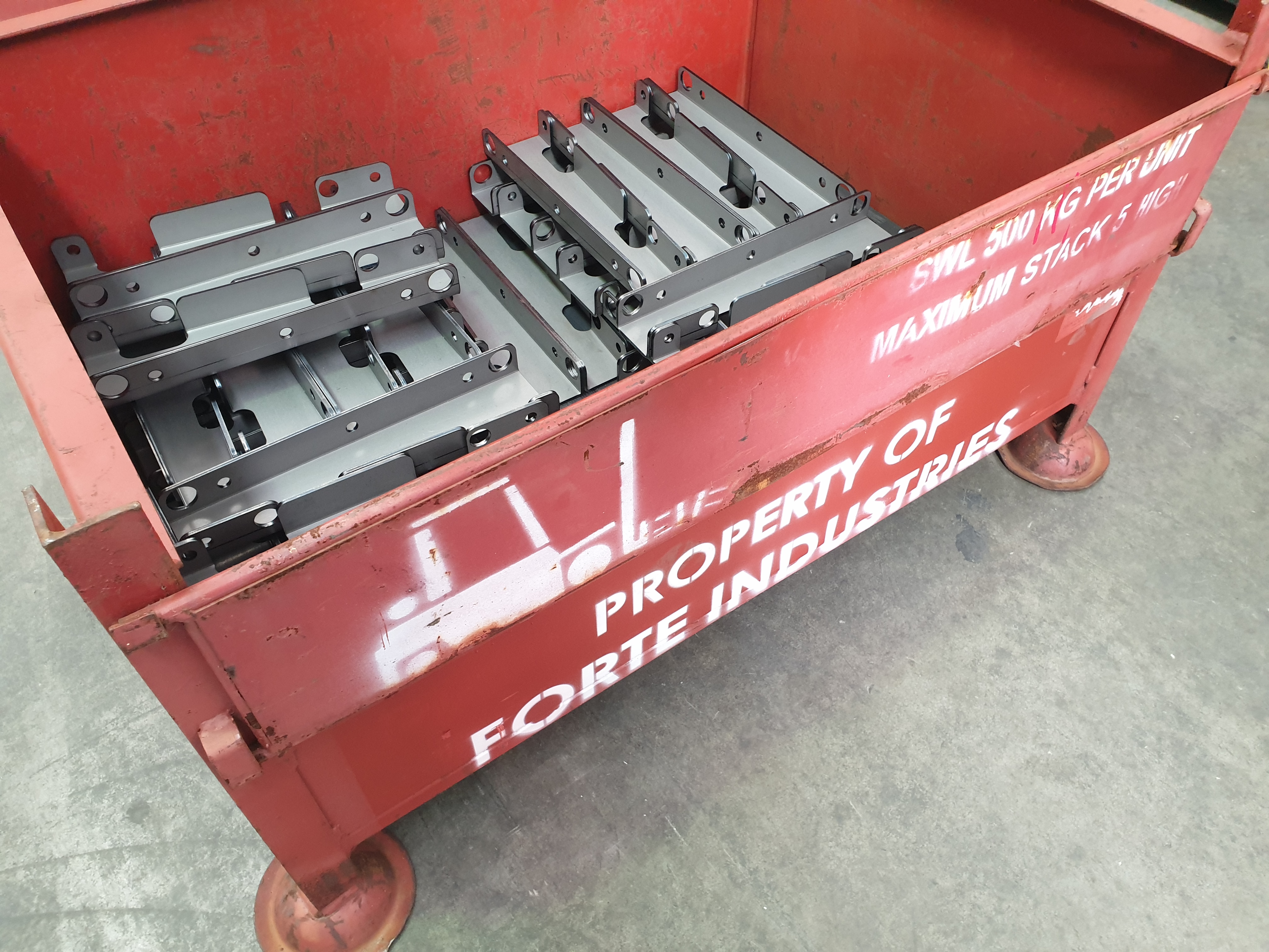 Red metal container with Forté Industries branding containing precision-manufactured metal components